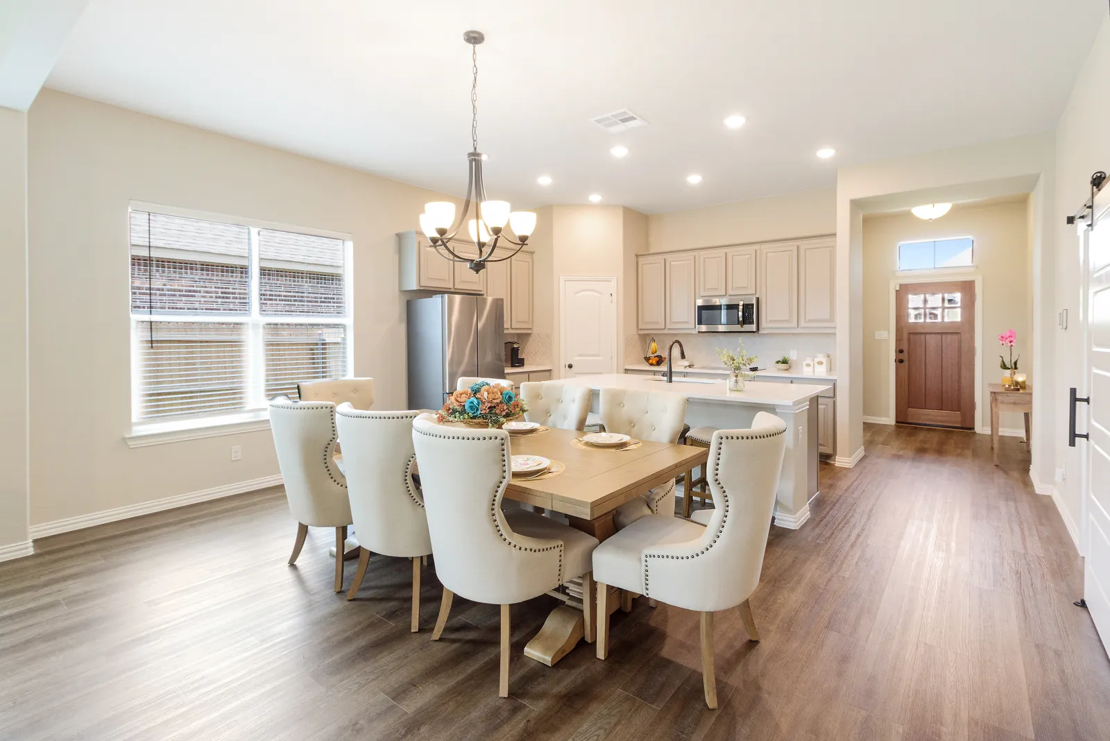 Dining area beside the kitchen under a chandelier, with the island and the front entry beyond