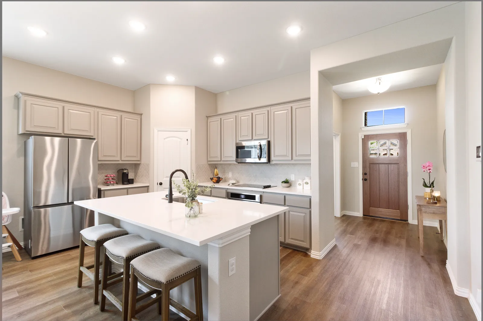 White kitchen with a quartz-topped island and three stools, stainless appliances and wood-look plank flooring